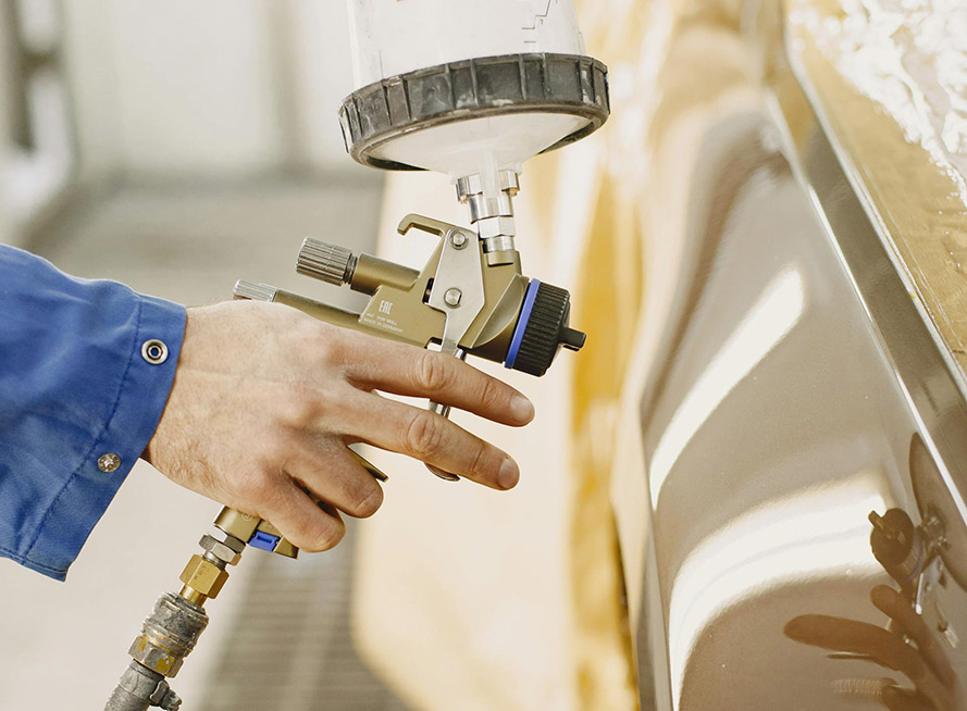 A person using a spray gun to apply paint to a car's surface in a well-lit garage setting.
