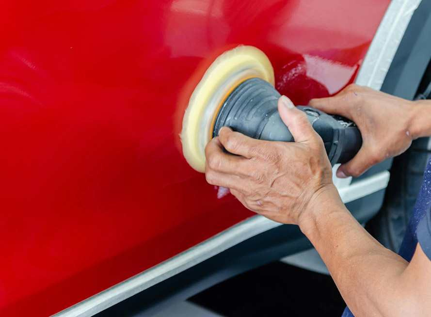 A man using a polisher to shine a red car, focusing on enhancing its glossy finish.
