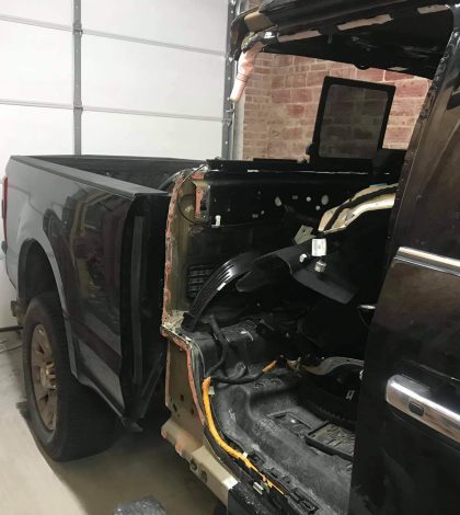 A partial view of a black truck with an exposed interior, parked in a garage with a closed door in the background.