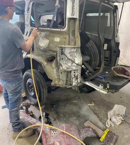 A man is repairing a vehicle inside a garage, surrounded by tools and equipment.