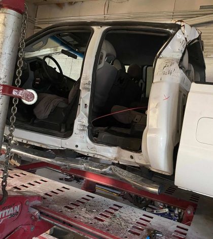 A white truck is elevated on a hydraulic lift in a garage setting.
