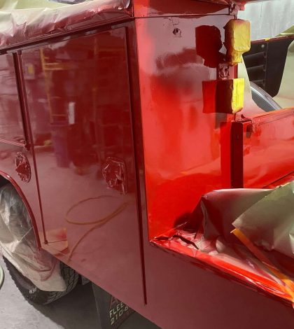 A red fire truck is being painted with green paint, showcasing a unique color transformation in progress.