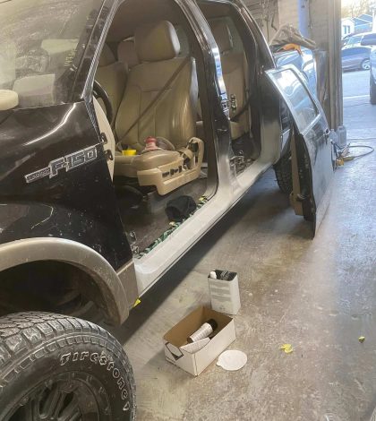 A truck is being repaired in a garage, with tools and equipment visible around the vehicle.