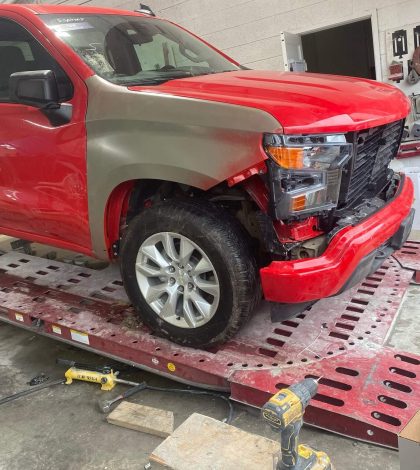 A red truck is being repaired in a garage, with tools and equipment visible around the vehicle.