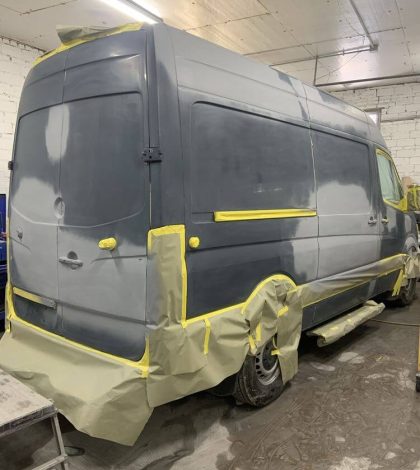 A van is being painted with yellow paint inside a garage.