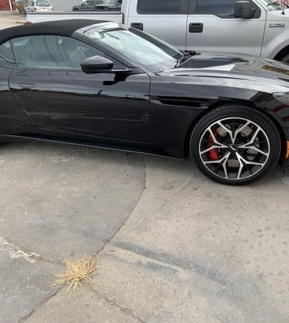 A black sports car parked in a parking lot, surrounded by other vehicles and clear blue sky in the background.