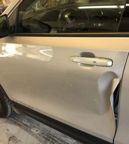 A silver car with a noticeable dent on the driver's side door.