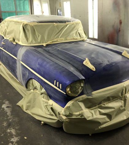 A blue car wrapped in plastic and splattered with paint, showcasing a creative and unconventional design.