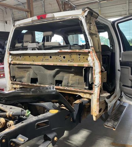A truck is being repaired inside a garage, with tools and equipment visible around the vehicle.